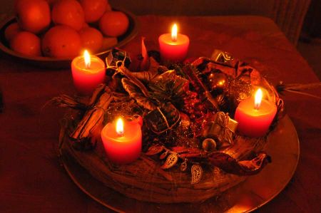 Holiday candle arrangement with red candles on a wooden plate surrounded by dried herbs and spices